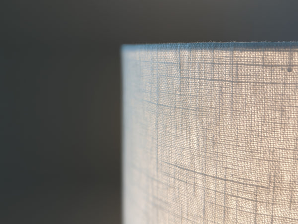 Close-up of a drum lampshade made of white linen fabric lit by a lightbulb