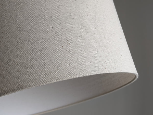 Speckled Oatmeal cotton fabric lampshade with brass hardware against a blurred background