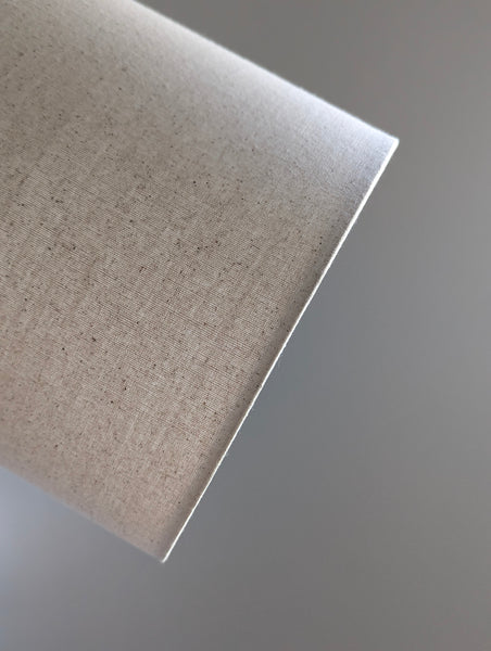 Speckled Oatmeal cotton fabric lampshade with brass hardware against a blurred background
