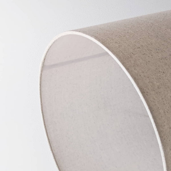 Speckled Oatmeal cotton fabric lampshade with brass hardware against a blurred background