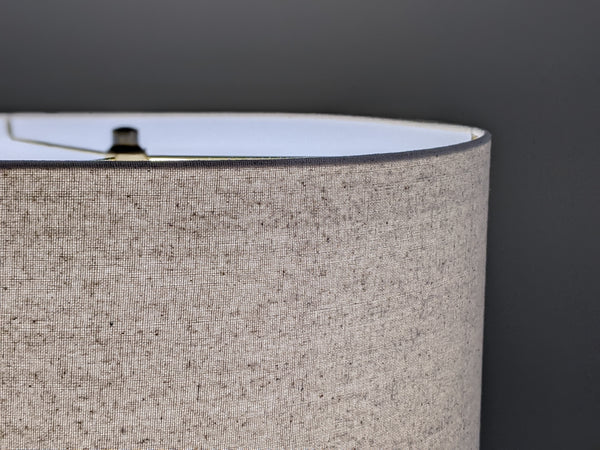 Speckled Oatmeal cotton fabric lampshade with brass hardware against a blurred background