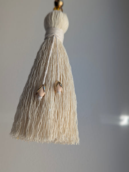 Beige tassel with brass and wooden beads on a plain background