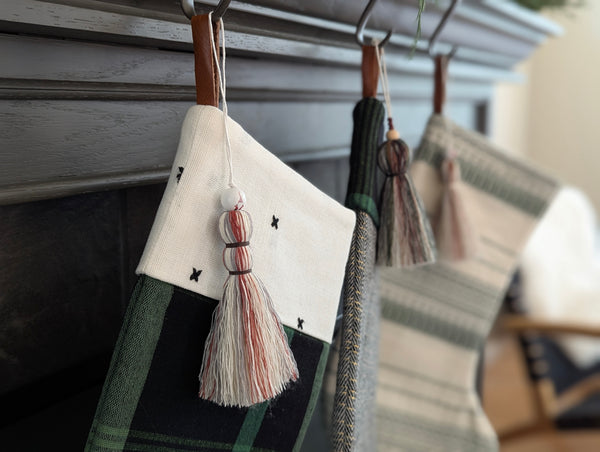 Three patterned stockings with tassels hanging on a fireplace mantle.