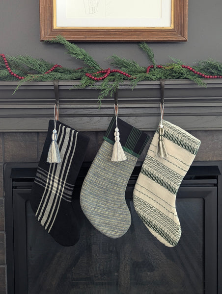 Three patterned stockings with tassel stocking charms hanging on a fireplace mantle.
