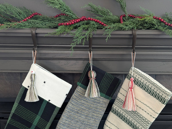 Three Christmas stockings with tassels hanging on a fireplace mantle decorated with greenery and berries.