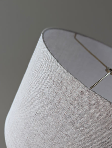 Close-up of a textured linen lamp shade with brass hardware against a blurred background