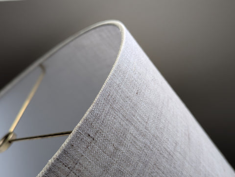 Close-up of a tan and gray linen lampshade with brass hardware against a blurred background
