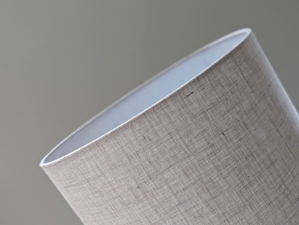 Close-up of a natural colored linen lampshade with brass hardware against a blurred background