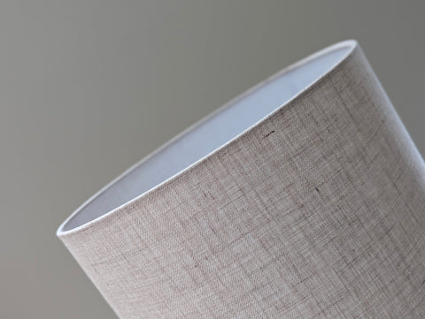 Close-up of a natural colored linen lampshade with brass hardware against a blurred background