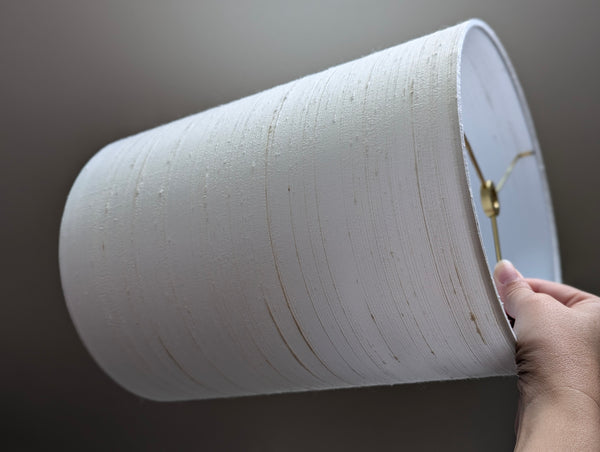 White silk lampshade with a hand holding it against a dark background