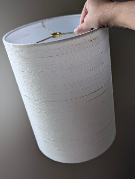 White silk lampshade with a hand holding it against a dark background