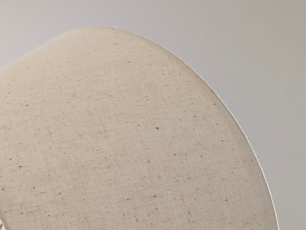 Close-up of a light beige textured fabric with small brown specks, shown on a curved surface against a neutral gray background.
