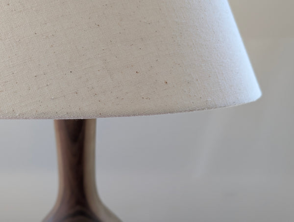 Close-up of a table lamp with a natural beige linen drum shade and a walnut lamp against a soft neutral background.