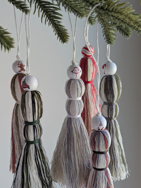 Holiday themed, decorative tassel ornaments hanging from a Christmas tree branch.