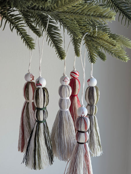 Holiday inspired, decorative tassel ornaments hanging from a Christmas tree branch.