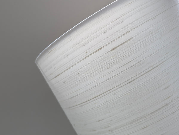 A close-up of a white drum lampshade  against a solid gray background.