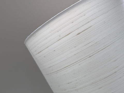 A close-up of a white drum lampshade  against a solid gray background.