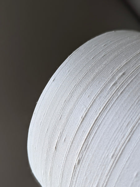 close up of a textured lamp shade with a hand holding it against a dark wall