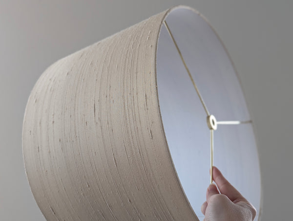 Close-up of a hand holding a silk lampshade on a plain background