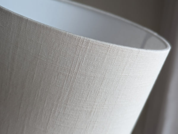 Close-up of a textured lampshade in white linen against a neutral background