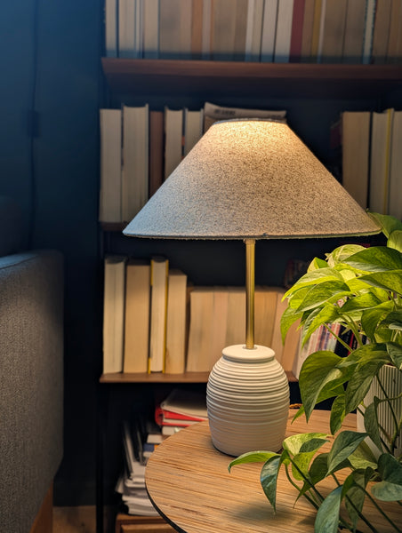 Table lamp with textured shade on a wooden table next to books and a plant