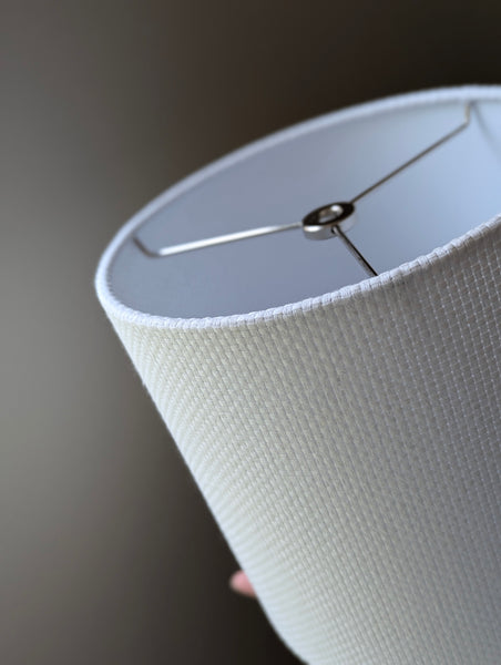 Close-up of a white textured lampshade with a visible woven pattern with nickel hardware