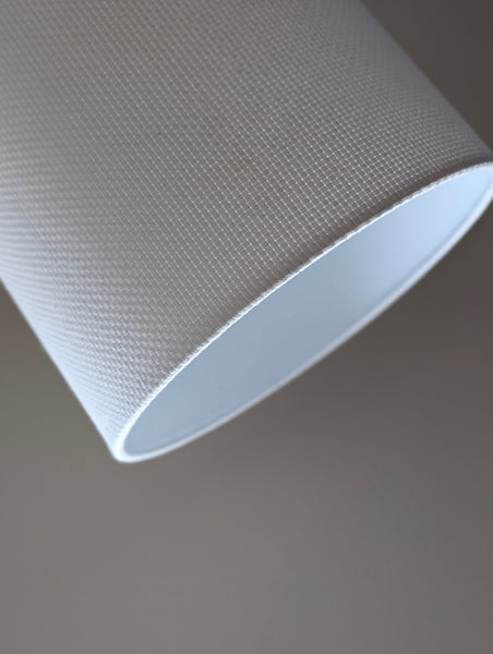 Close-up of a white textured lampshade in Bright White Crosshatch fabric against a soft gray background