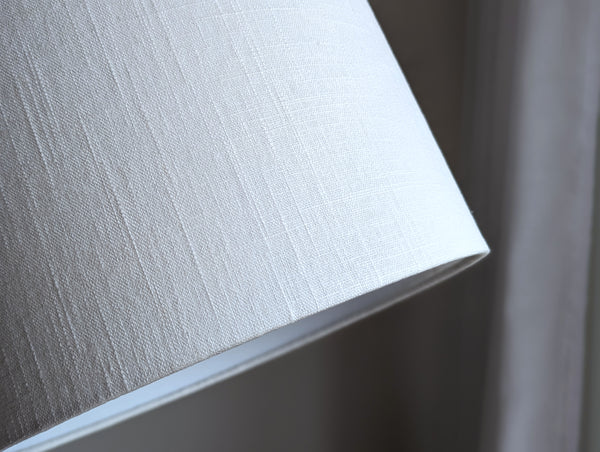 Close-up of a textured lamp shade in white linen fabric against a neutral background