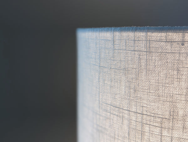 Close-up of a white linen lamp shade lit by a light bulb with light shining through tit