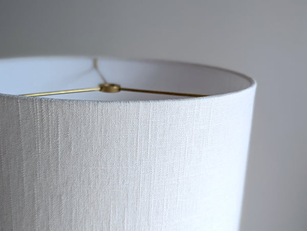 Close-up of a white linen lamp shade with brass spider washer hardware against a neutral background