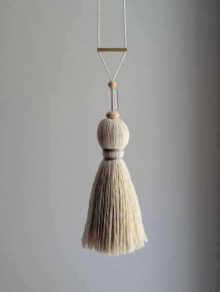 Decorative tassel with wooden and glass beads and a brass bar on a gray background