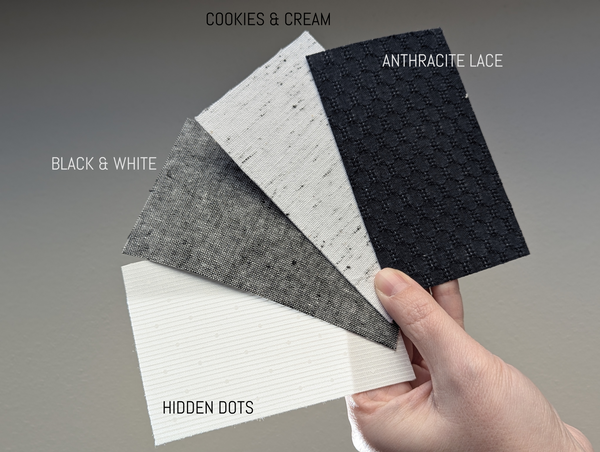 Hand holding fabric swatches labeled 'Cookies & Cream', 'Anthracite Lace', 'Black & White', and 'Hidden Dots' against a gray background.