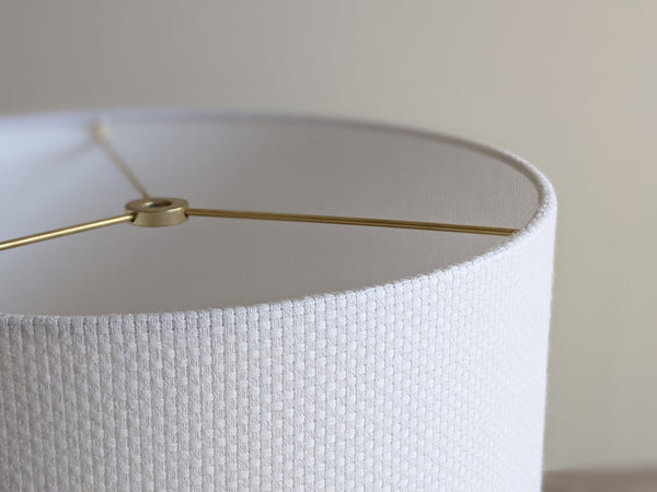 Close-up of a white textured lampshade with a visible woven pattern with brass hardware