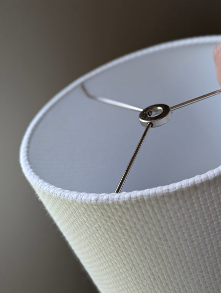 Close-up of a white textured lampshade with a visible woven pattern with nickel hardware