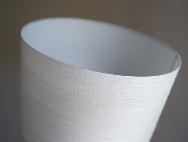 A close-up of a white textured silk lampshade, showing the inner surface and the fine horizontal ribbed texture against a neutral gray background.