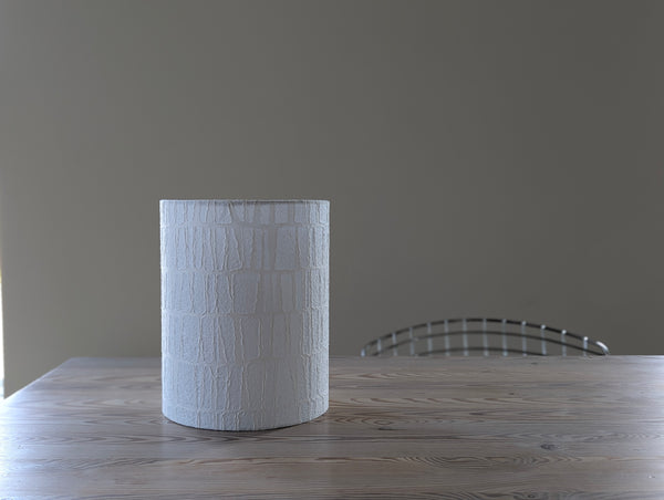 white paper textured lamp shade with rectangle pattern sitting on a light wood table