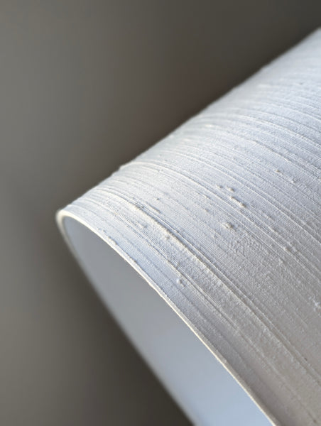 Close-up of a white textured drum lamp shade in textured silk against a neutral gray background.