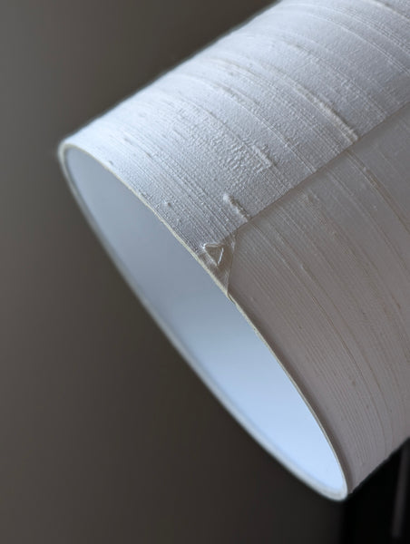 Close-up of a white textured silk lampshade against a dark gray background.