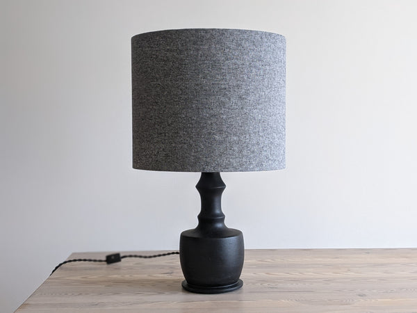 a black and white fabric lampshade that appears grey is on a black table lamp sitting on a light wood table