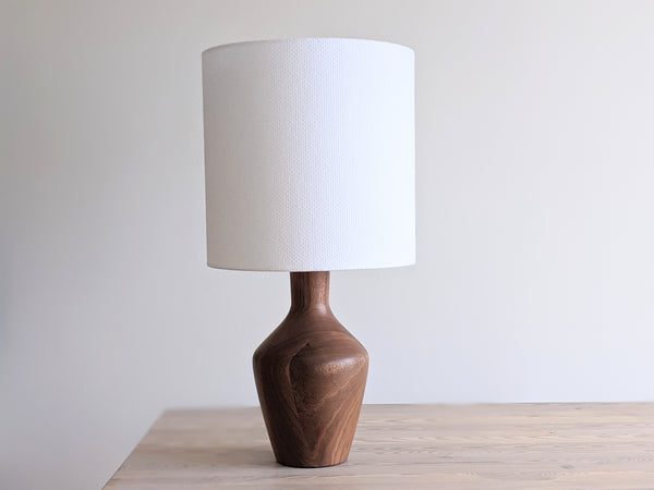 Bright white crosshatch fabric lamp shade on walnut table lamp sitting on a light wood table.