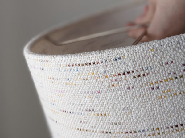 close up image of hand holding a custom lamp shade in handwoven Confetti fabric