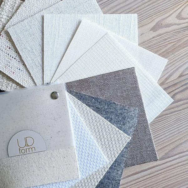 sample book laying on a table with Ud Form custom lamp shade fabrics in whites, creams, naturals, brown, grey, and multi-color
