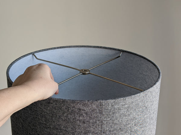 a hand is holding a grey fabric lamp shade by the top spider ring nickel hardware