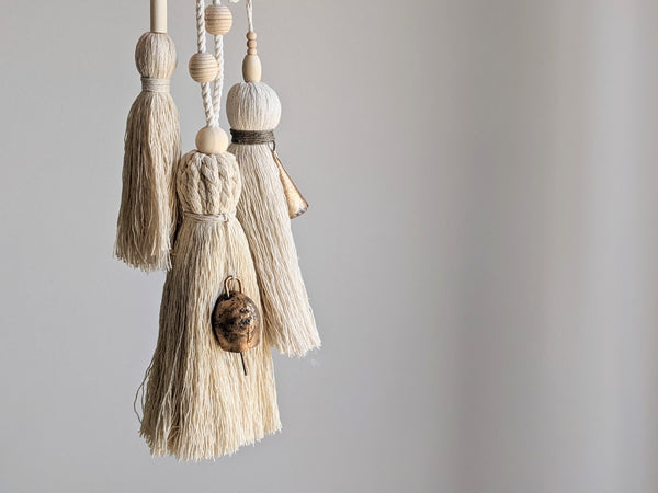 Three natural cotton tassels with wooden beads and brass bells hanging in a cluster