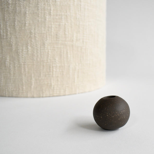 The cream boucle lampshade and dark brown glazed ceramic finial have been removed from the lamp and are sitting next to each other.