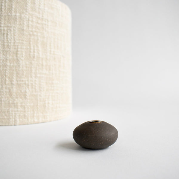 The cream boucle lampshade and dark brown glazed ceramic finial have been removed from the lamp and are sitting next to each other.