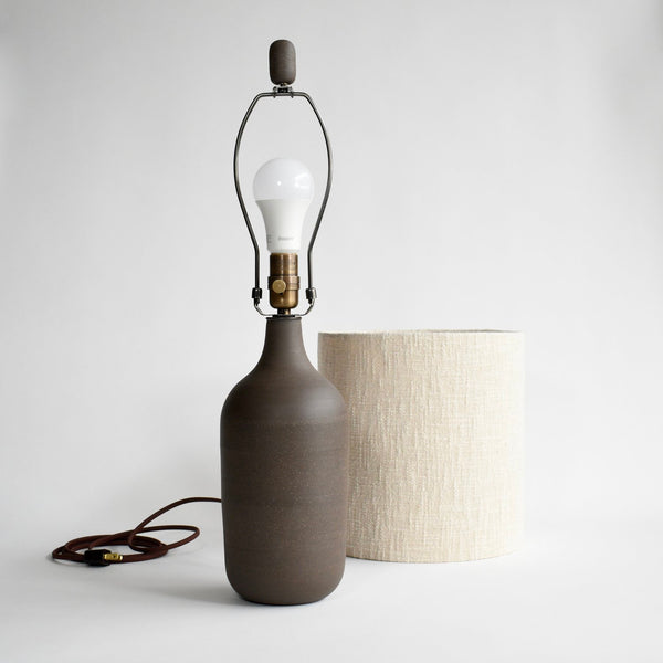 The dark brown, peat glazed ceramic lamp has the shade removed and sitting next to it. This shows off the matching ceramic finial at the top of the ceramic table lamp.