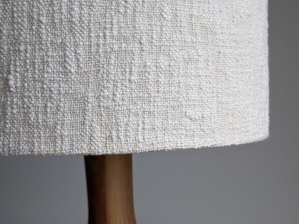 close up image of nubby fibers on an natural cotton handwoven fabric lamp shade that sits on a walnut table lamp
