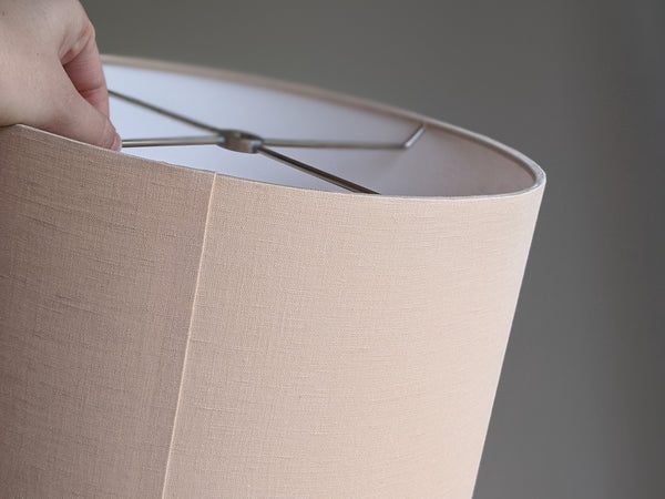 Close up of hand holding a handmade blush linen lampshade showing the back and seam detail of the lamp shade.