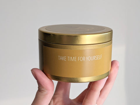 gold candle tin labelled "Take Time For Yourself' being held in the sun